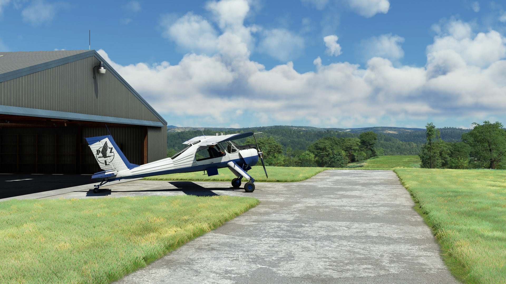 The Got Friends Wilga sits in front of a metal hangar with asphalt pavements surrounded by green grass