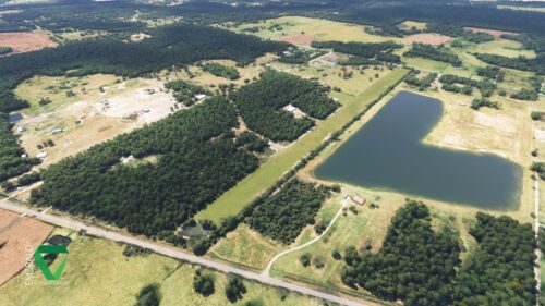 An aerial view of a green striped grass runway with an L shaped lake next to it