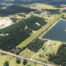 An aerial view of a green striped grass runway with an L shaped lake next to it